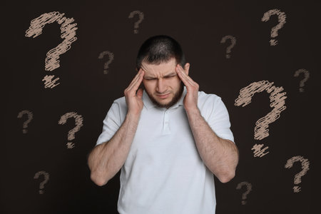Amnesia. Confused man and question marks on brown backgroundの写真素材