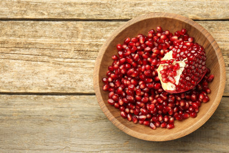 Ripe juicy pomegranate grains in bowl on wooden table, top view. Space for textの写真素材