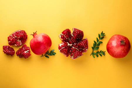 Fresh pomegranates and green leaves on yellow background, flat layの写真素材