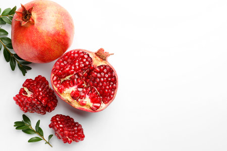 Fresh pomegranates and green leaves on white background, flat lay. Space for textの写真素材