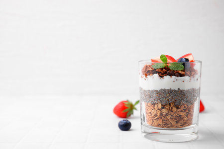 Tasty granola with berries, yogurt and chia seeds in glass on white tiled table, space for textの写真素材