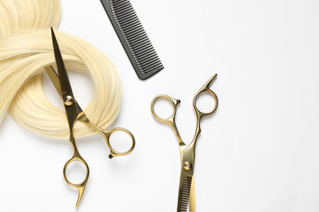 Professional hairdresser scissors and comb with blonde hair strand on white background, flat layの写真素材