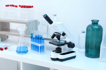 Laboratory analysis. Different glassware with blue liquid and microscope on white table indoorsの写真素材