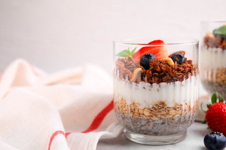 Tasty granola with berries, nuts, yogurt and chia seeds in glass on white table, space for textの写真素材