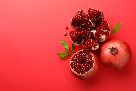 Fresh pomegranates and green leaves on red background, flat lay. Space for textの写真素材