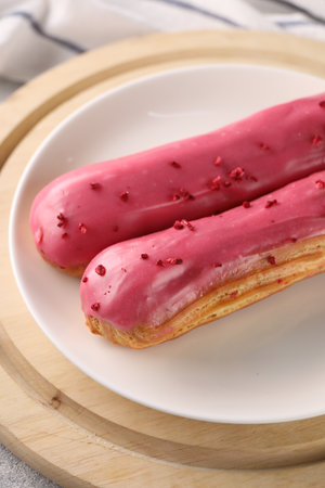 Plate with tasty glazed eclairs on wooden board, closeupの写真素材