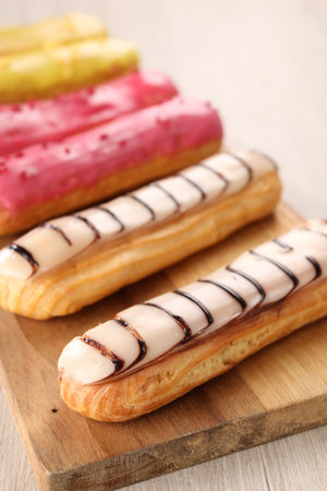 Board with different tasty glazed eclairs on light wooden table, closeupの写真素材