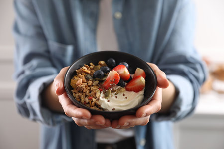 Woman holding bowl of tasty granola with berries, yogurt and seeds indoors, closeupの写真素材