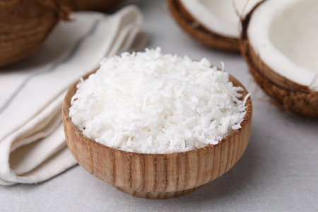 Coconut flakes in bowl and nut on light gray table, closeupの写真素材
