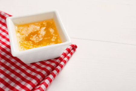 Melted butter in bowl on white wooden table, closeup. Space for text