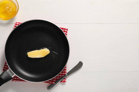 Melting butter in frying pan and knife on white wooden table, top view. Space for textの写真素材