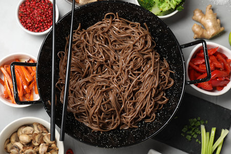 Wok with noodles, chicken and other products on light gray table, flat layの写真素材