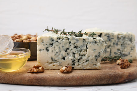 Tasty blue cheese with thyme, honey and walnuts on white table, closeup