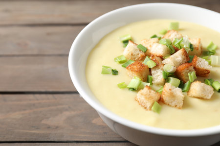 Tasty potato soup with croutons and green onion in bowl on wooden table, closeup. Space for textの写真素材