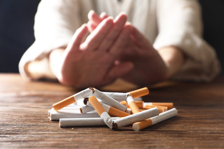 Stop smoking. Woman making stop gesture at wooden table, focus on whole and broken cigarettesの写真素材