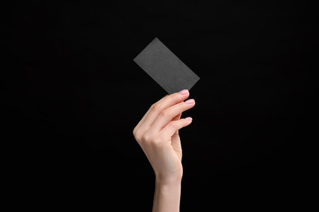 Woman holding blank business card on black background, closeup. Space for textの写真素材