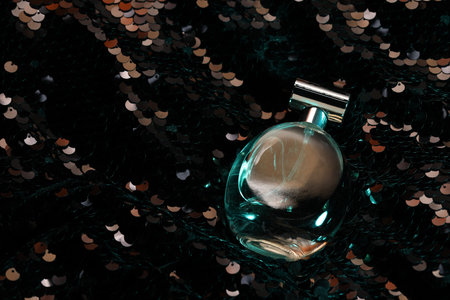 Luxury perfume in bottle on fabric with shiny sequins, above view