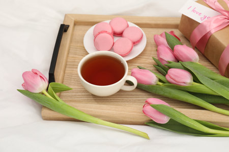 Tasty breakfast served in bed. Delicious macarons, tea, flowers, gift box and card with phrase I Love You on trayの写真素材
