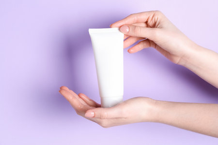 Woman holding tube of cream on violet background, closeupの写真素材