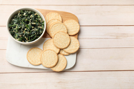 Tasty spinach dip with eggs in bowl and crackers on light wooden table, top view. Space for textの写真素材