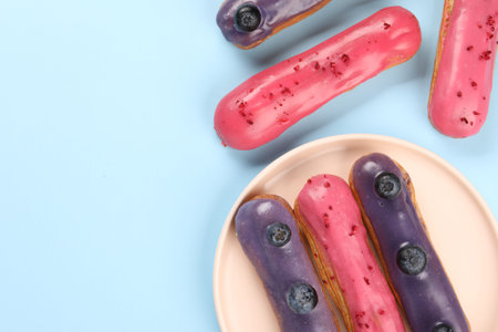 Delicious eclairs covered with glaze on light blue background, top view. Space for textの写真素材