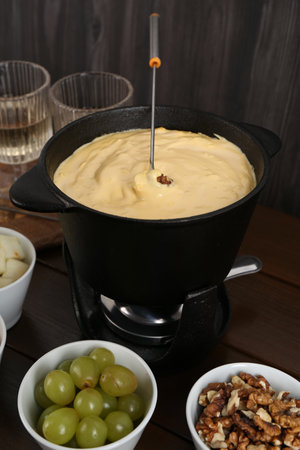 Fondue pot with tasty melted cheese, fork and different snacks on wooden tableの写真素材