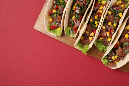 Delicious tacos with meat and vegetables on red table, top view. Space for text