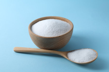 Organic white salt in bowl and spoon on light blue backgroundの写真素材