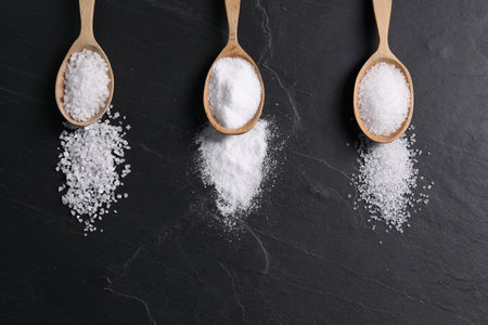 Natural salt and wooden spoons on black table, flat lay. Space for textの写真素材