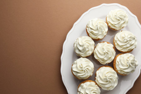Tasty vanilla cupcakes with cream on dark beige background, top view. Space for textの写真素材