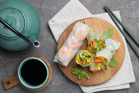 Tasty spring rolls served on gray textured table, flat lay