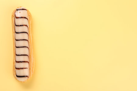 Delicious eclair covered with glaze on yellow background, top view. Space for text