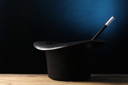 Magician's hat and wand on wooden table against dark backgroundの写真素材