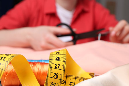 Woman cutting sewing thread over cloth, focus on measuring tape and spool threads