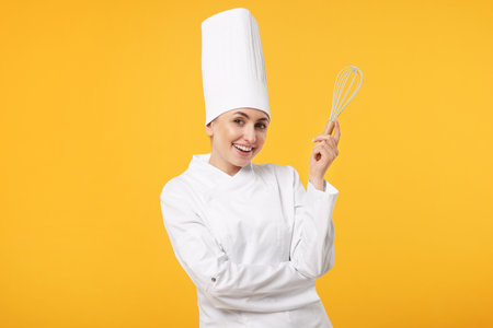 Happy professional confectioner in uniform holding whisk on yellow backgroundの写真素材