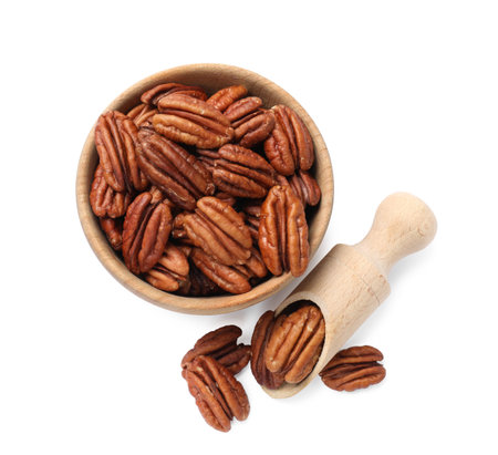 Tasty pecan nuts in bowl and scoop isolated on white, top view
