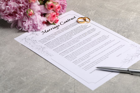 Marriage contract, golden wedding rings, pen and flowers on gray tableの写真素材