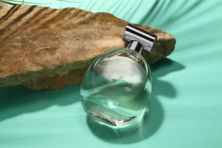 Bottle of luxury perfume in sunlight and stone on turquoise background