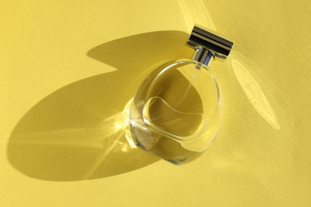 Luxury women's perfume. Sunlit glass bottle on yellow background, top viewの写真素材