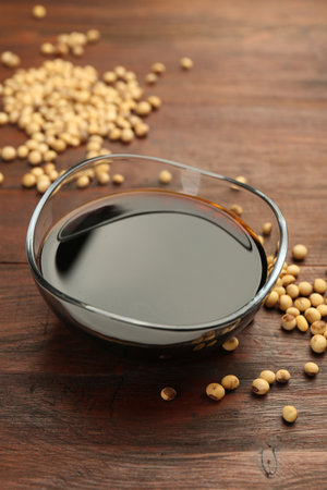 Soy sauce in bowl and soybeans on wooden tableの写真素材