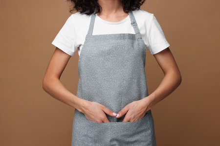 Woman wearing kitchen apron on brown background, closeup. Mockup for designの写真素材