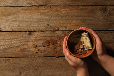 Donate and give concept. Woman holding bowl with coins and dollar banknotes at wooden table, top...