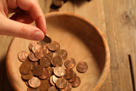 Donate and give concept. Woman putting coin into bowl at table, closeupの写真素材