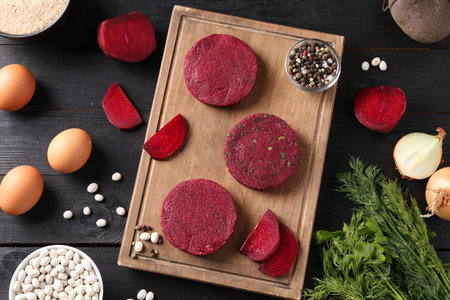 Uncooked beetroot cutlets and ingredients on black wooden table, flat lay. Vegetarian productの写真素材