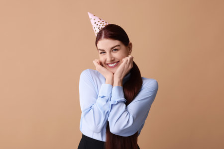 Happy woman in party hat on beige backgroundの写真素材