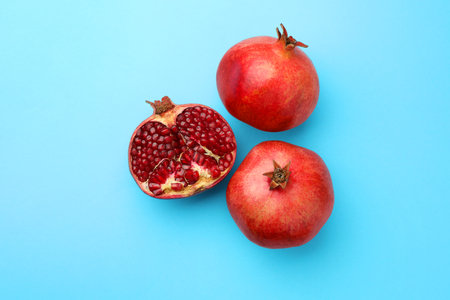 Whole and cut fresh pomegranates on light blue background, flat layの写真素材