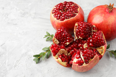 Fresh pomegranates and green leaves on gray textured table, space for textの写真素材