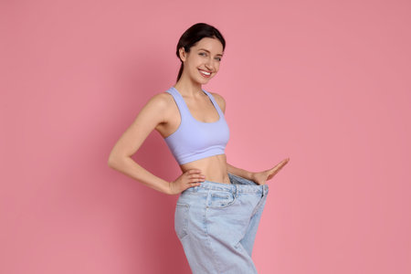 Happy young woman in big jeans showing her slim body on pink backgroundの写真素材