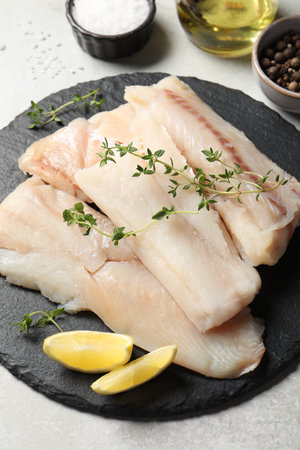 Pieces of raw cod fish, lemon and spices on light gray tableの写真素材