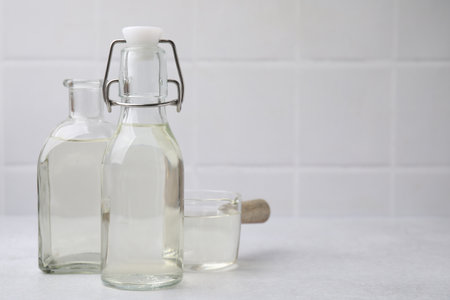 Vinegar in glass bottles and saucepan on light table, space for text